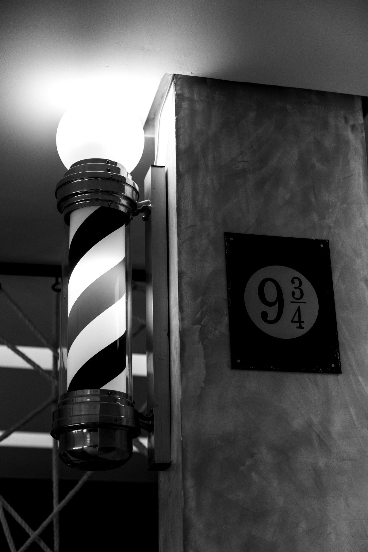 Interior da Barbearia 9¾: barber pole iluminado ao lado da placa oval 9¾ na parede de concreto