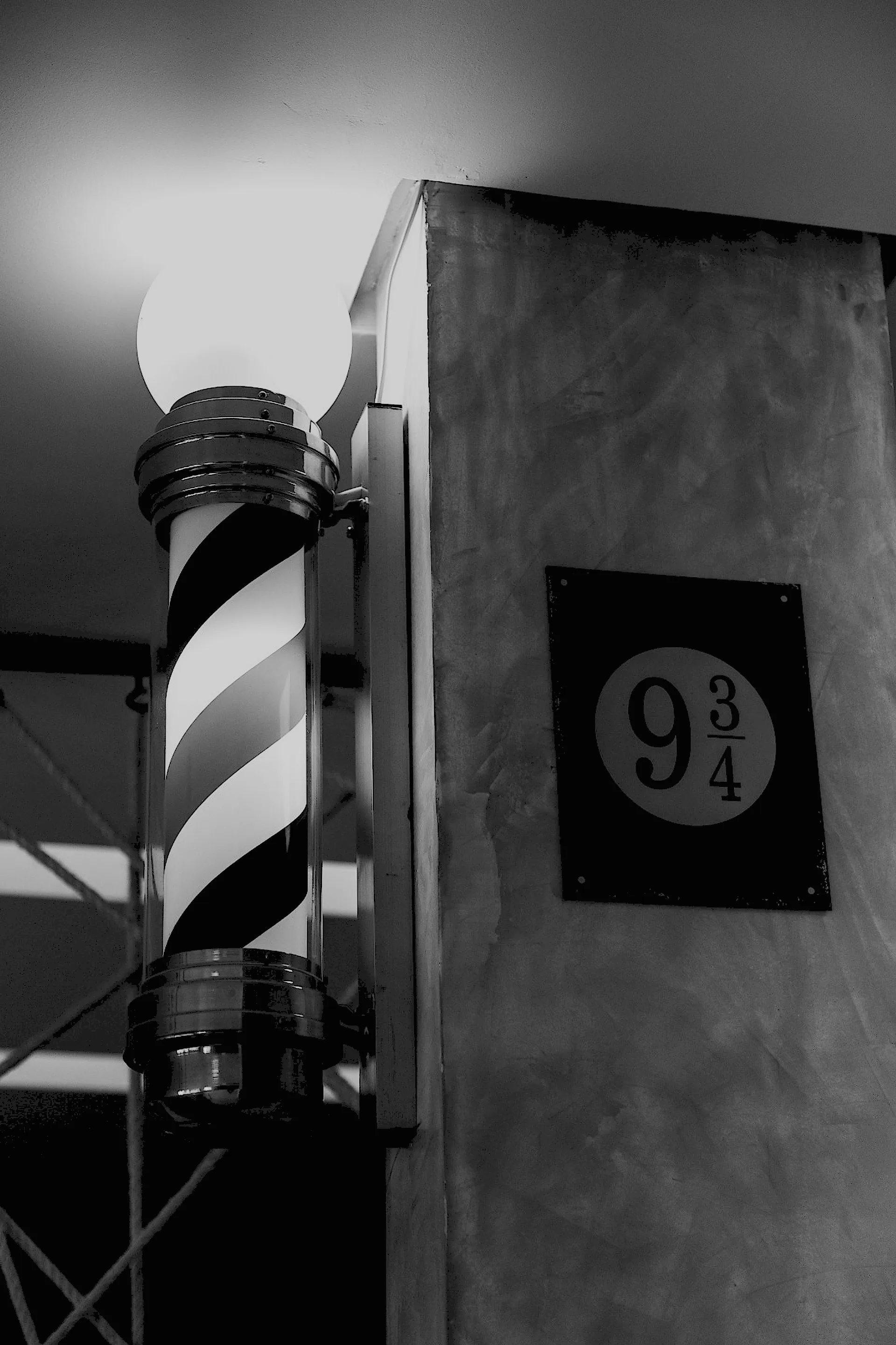 Barber pole aceso ao lado da placa oval 9¾ na parede de concreto do salão